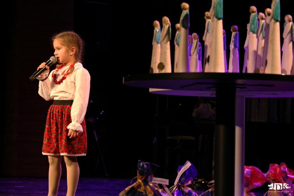 dziewczynka w ludowym stroju z czerwonymi kokardkami w warkoczach i czerwonych koralach