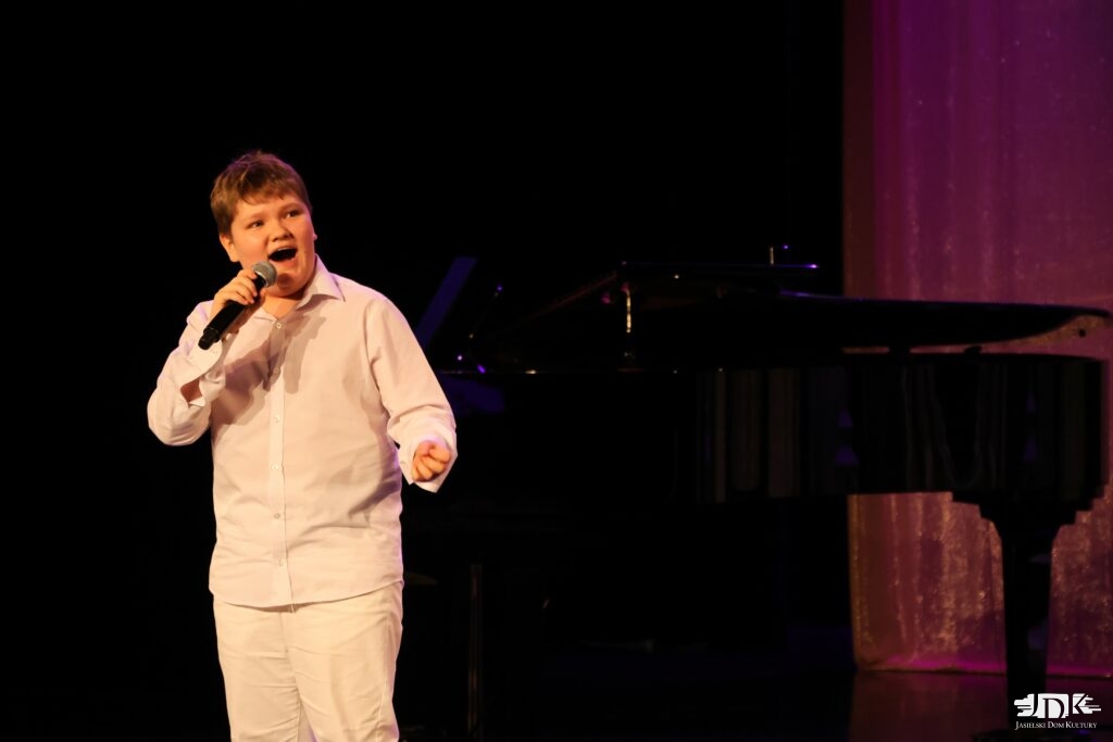 zdobywca grand prix w białym stroju śpiewa do mikrofonu