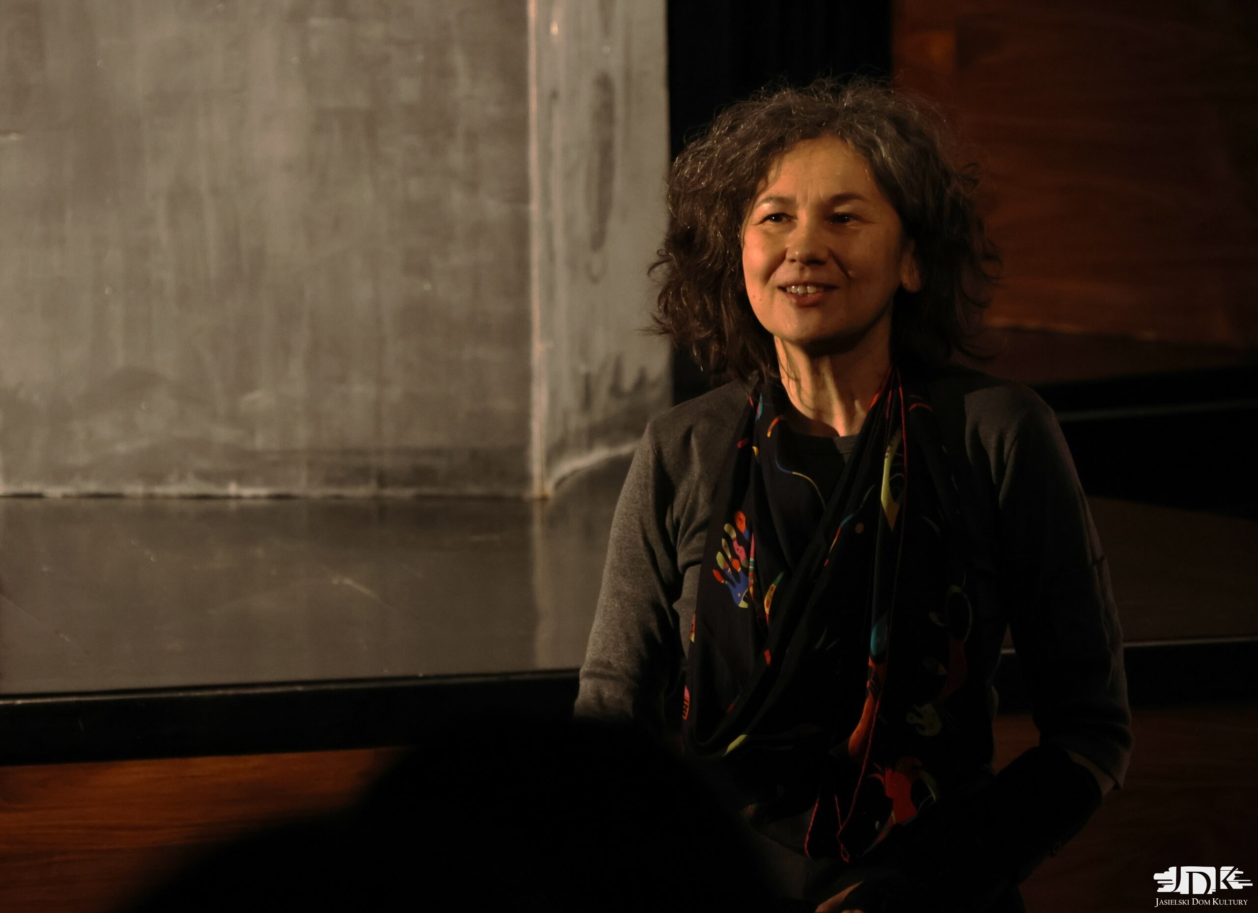 instruktorka teatru dla młodzieży w szarym sweterku uśmiechająca się do kamery