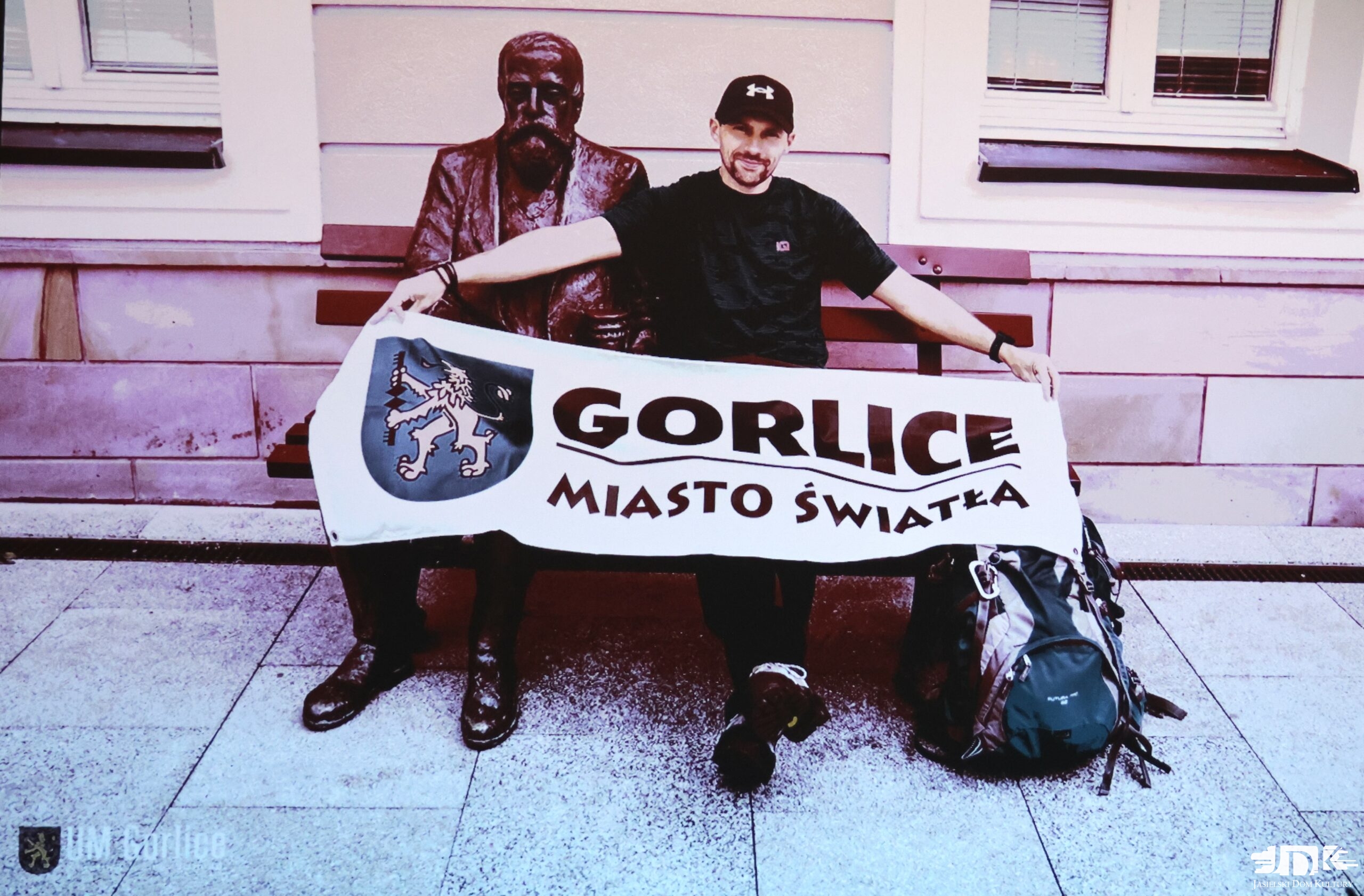 bohater spotkania trzymający flagę z napisem "gorlice miasto światła", siedzący na ławeczce przy pomniku Łukasiewicza