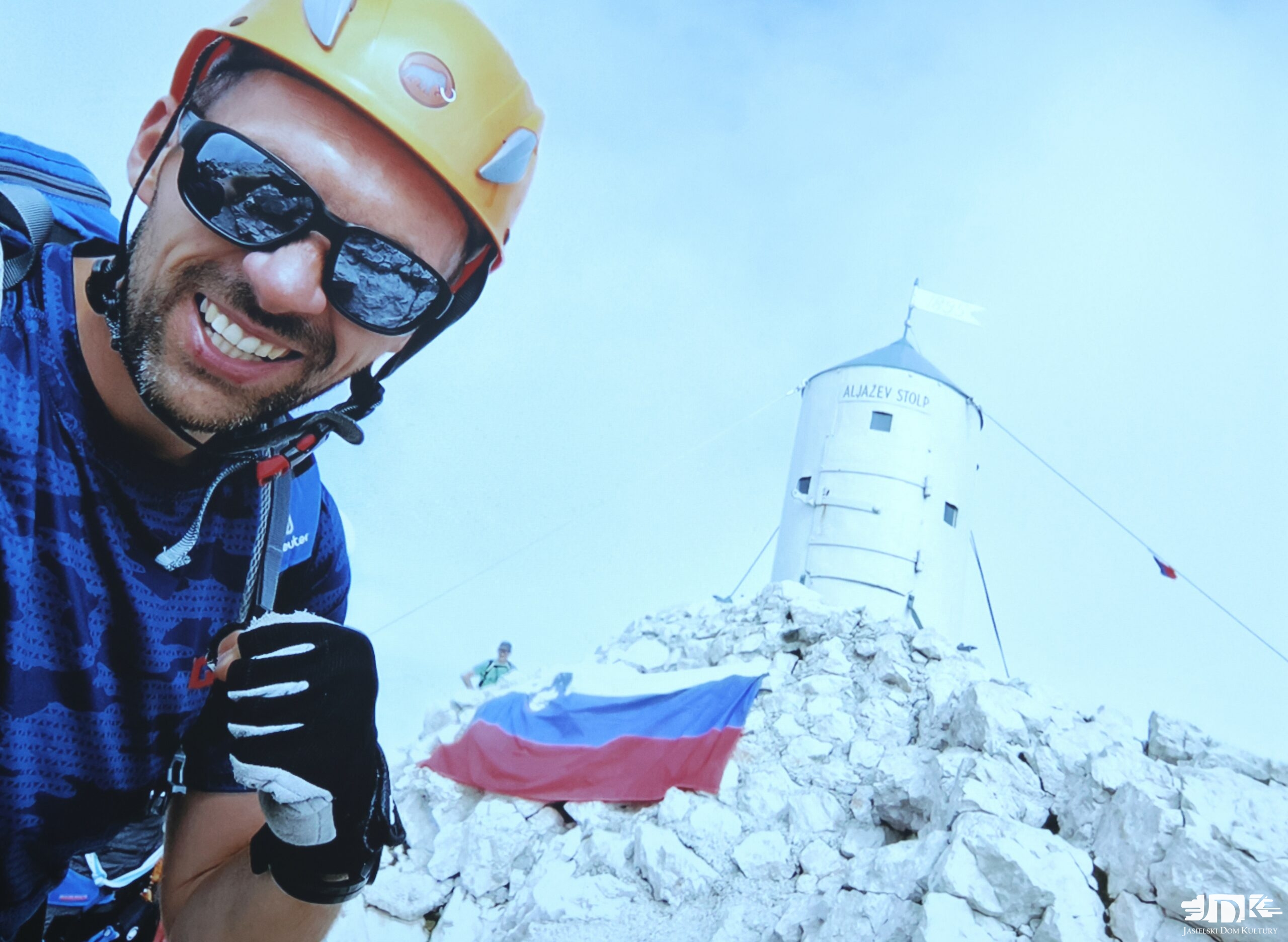 bohater spotkania w kasku i okularach przeciwsłonecznych, w tle burzochron na szczycie