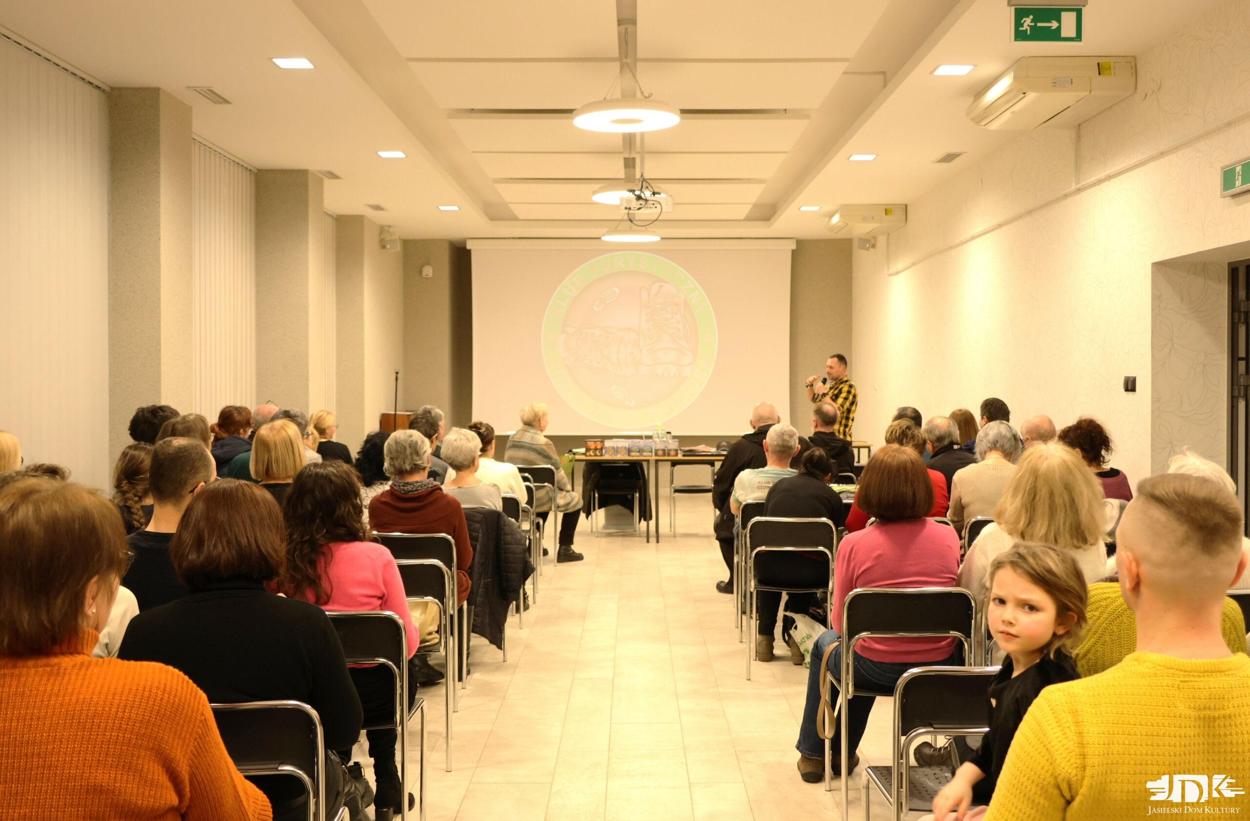 liczne grono uczestników spotkania siedzi na krzesłach tyłem do obiektywu