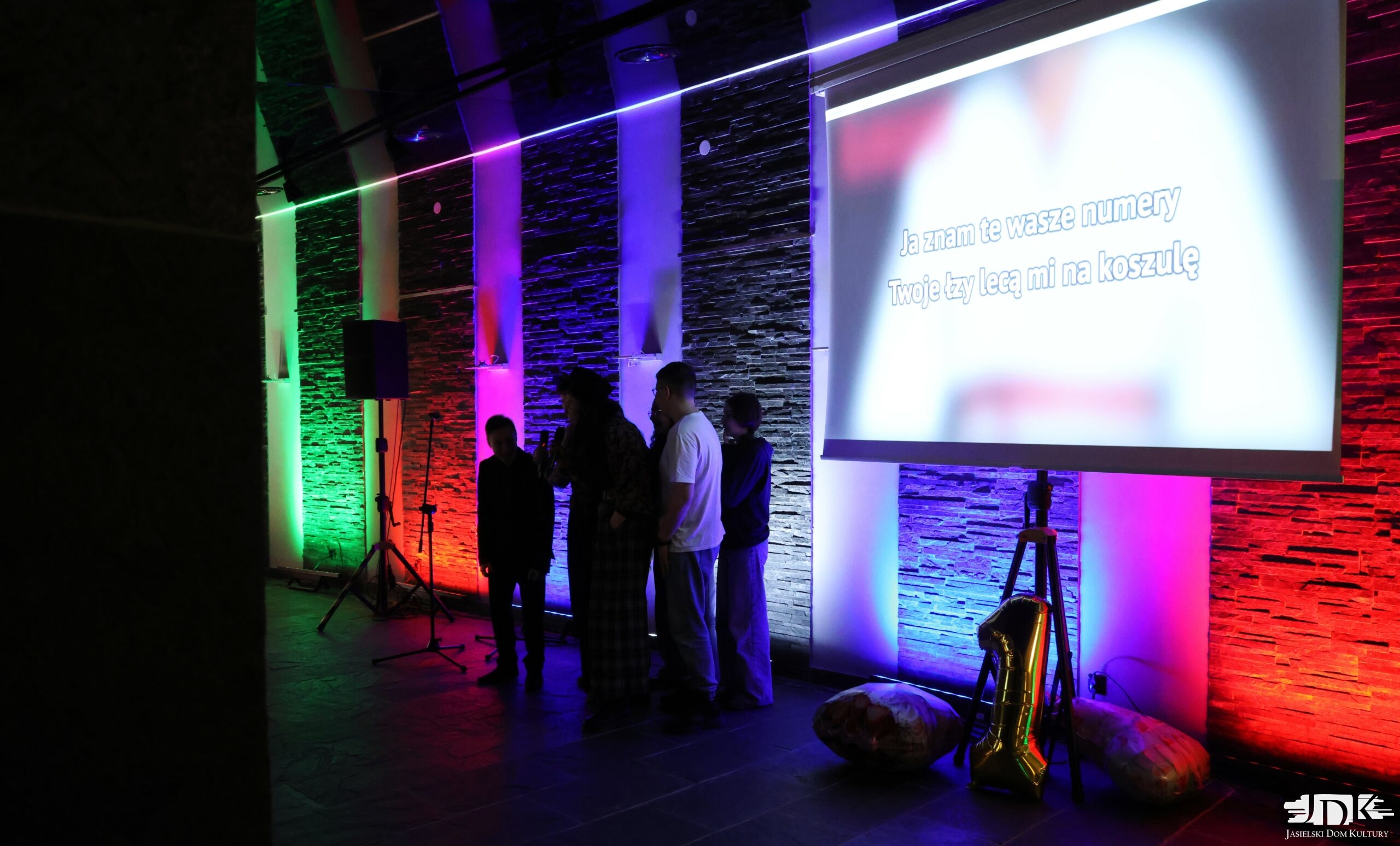 grupka młodzieży oraz ekran wyświetlający tekst piosenki "king bruce lee karate mistrz"