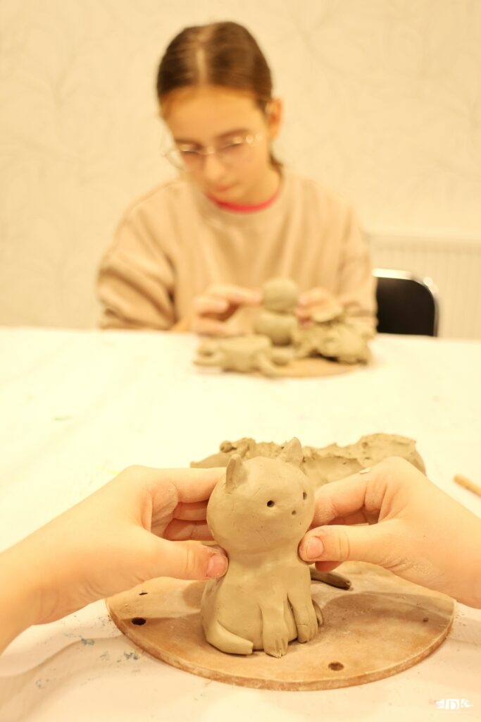 na pierwszym planie kot z gliny, w tle dziewczynka