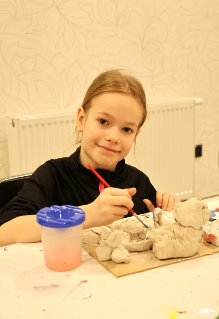 uśmiechnięta dziewczynka patrząca w obiektyw, z pędzlem w dłoni