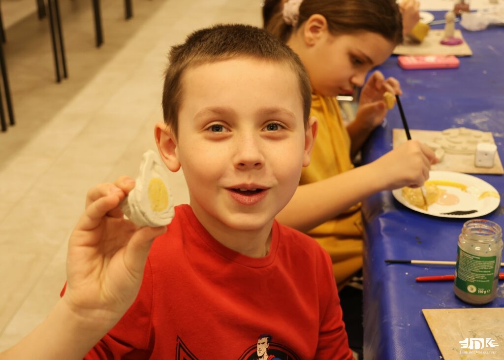 uśmiechnięty chłopiec pokazujący do obiektywu rzeźbę kostkę