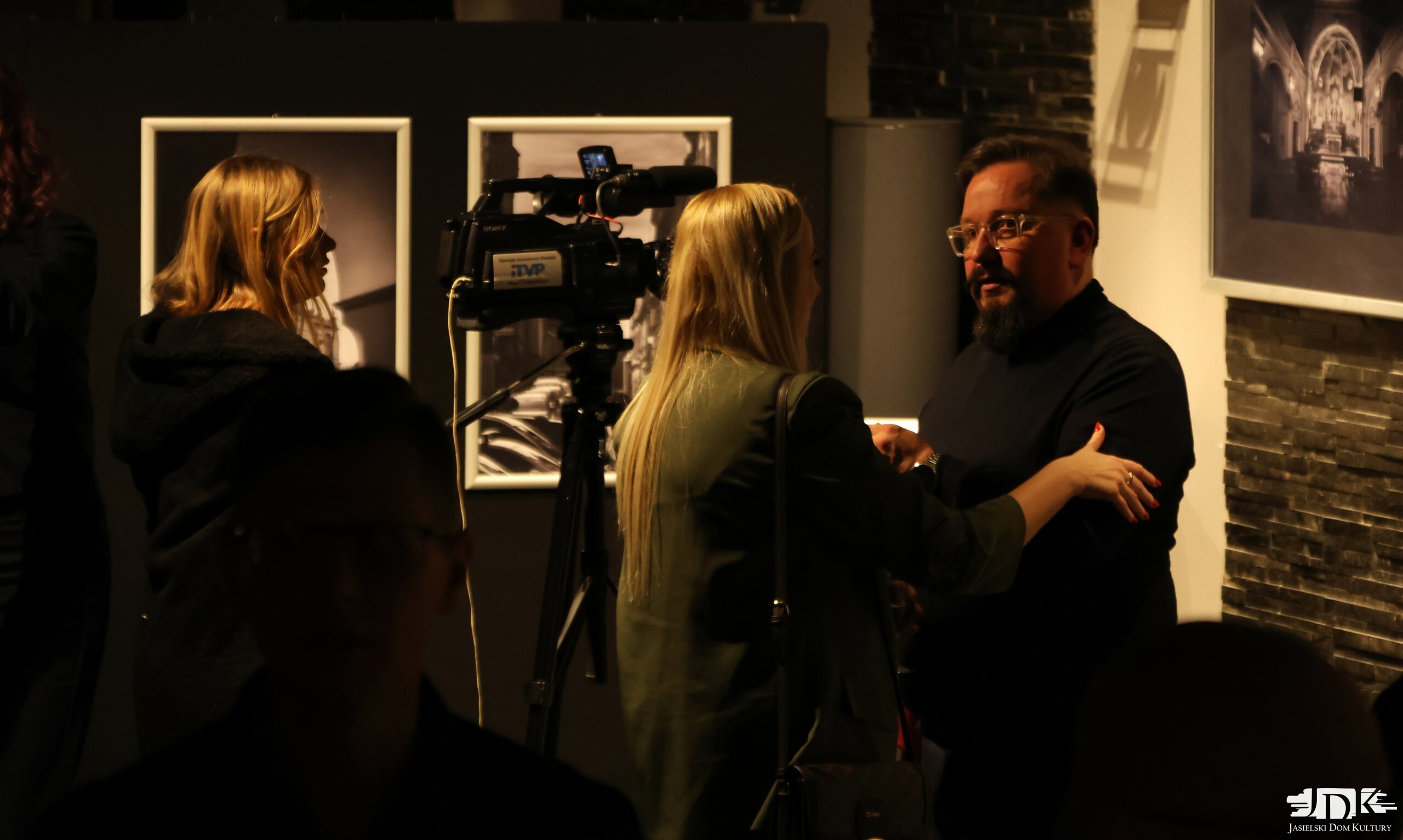 autor wystawy udziela wywiadu przed kamerą, kobieta łapie go za rękę, witając się