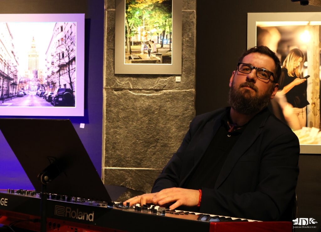 pianista patrzy w obiektyw, za nim obrazy - fotografie