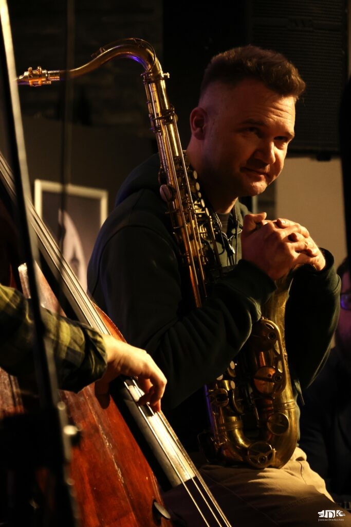 uśmiechnięty saksofonista siedzący za kontrabasem