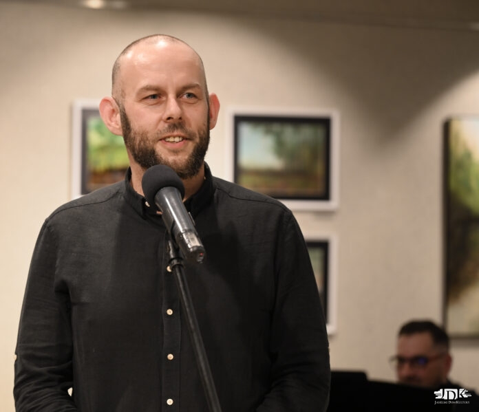 DSC_4278 (1) Mężczyzna z brodą , artysta Bartłomiej Smyka stoi przed mikrofonem, gotowy do wystąpienia