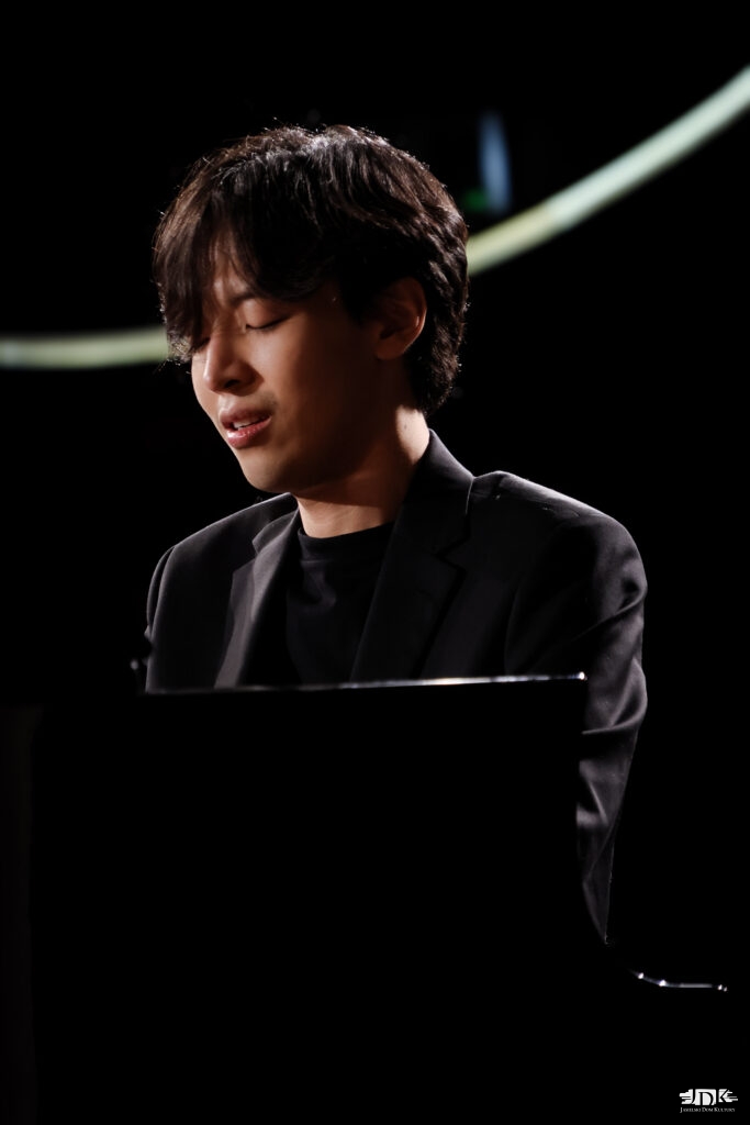 artysta z lekkim uśmiechem grający na fortepianie