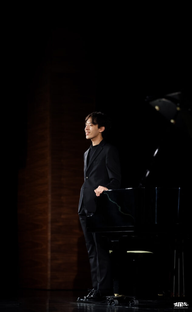 uśmiechnięty Hyuk Lee stojący przy fortepianie
