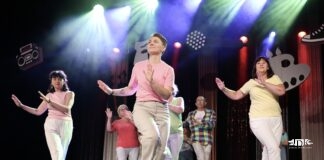 Sobota na Kołłątaja 1 – zakończenie sezonu artystycznego Grupa dorosłych w kolorowych koszulkach wykonuje układ taneczny na oświetlonej scenie teatralnej.