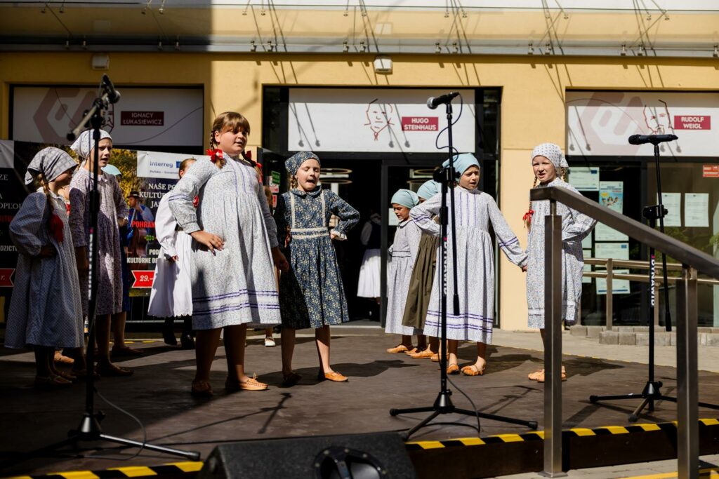 zespół pieśni i tańca w tradycyjnych strojach, tańczący przed budynkiem 