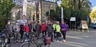Jesienne refleksje z Zespołu Parkowo-Dworskiego i Folwarcznego w Wiśniowej grupa trzynastu rowerzystów pod budynkiem JDK - w kaskach oraz sportowym ubraniu