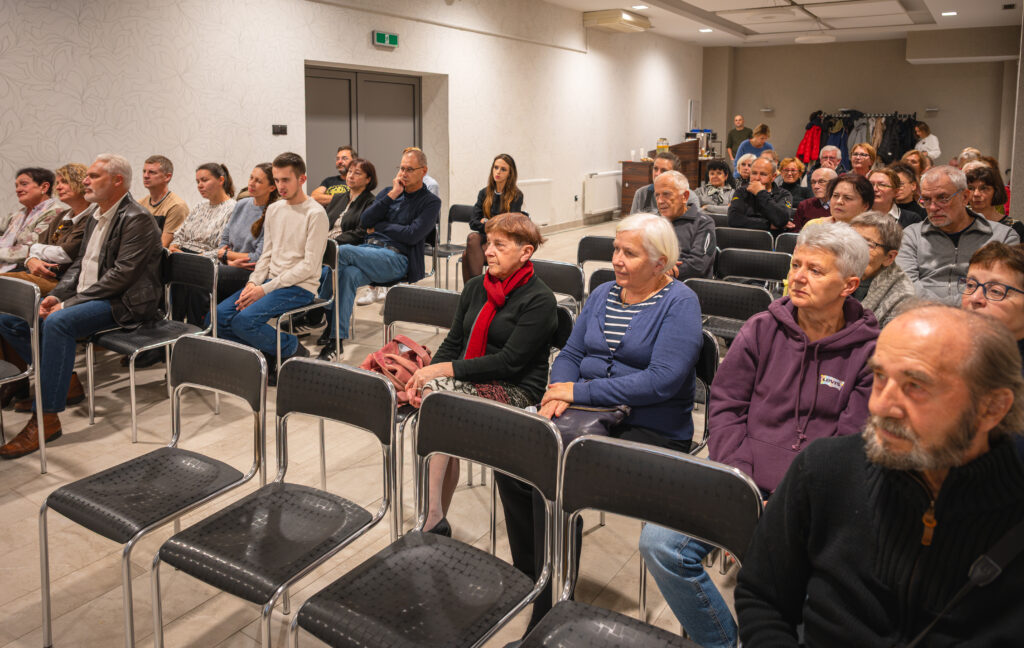 Uczestnicy spotkania siedzą na krzesłach w sali konferencyjnej i słuchają wystąpienia.